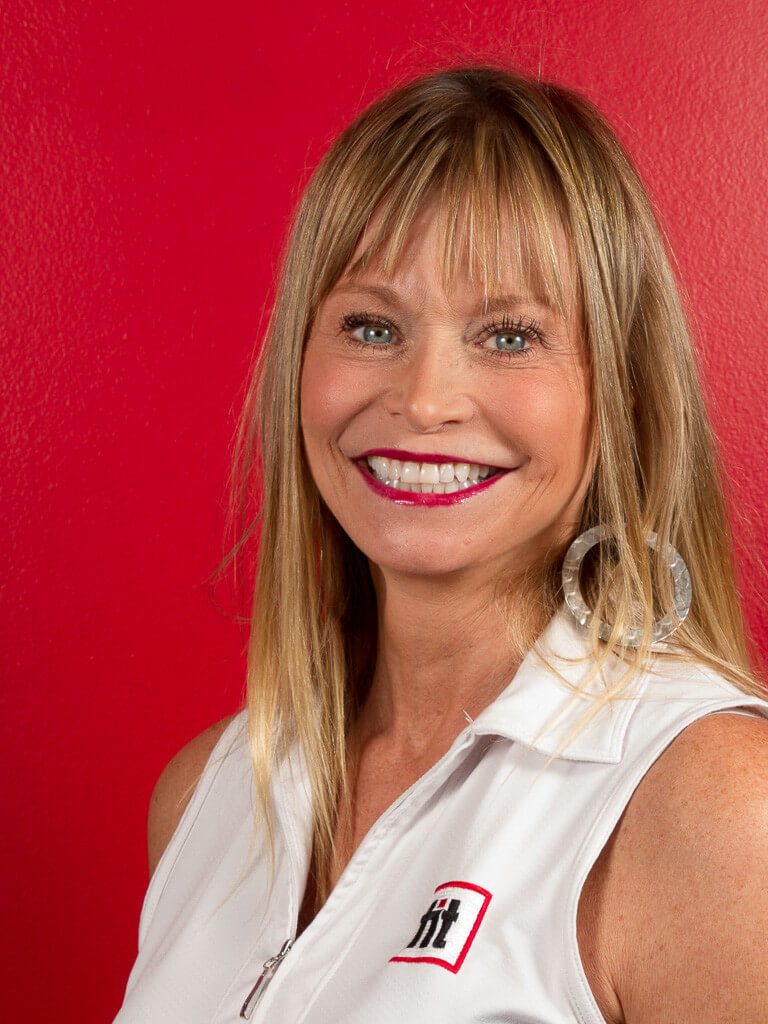 Smiling blonde woman wearing a white sleeveless collared shirt stands in front of a red background.